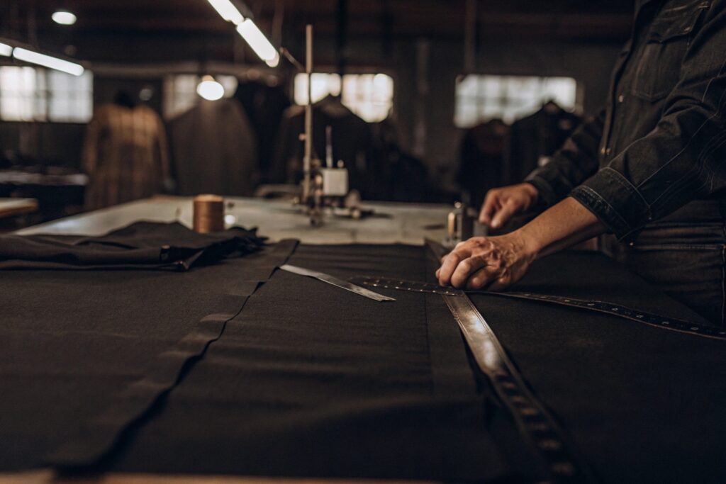 Tailor measuring and cutting dark fabric in a garment workshop