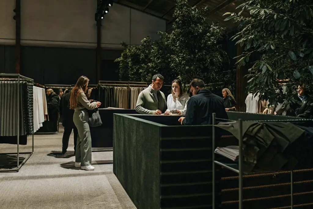 A bustling international trade fair where clothing manufacturers and fashion brands network and explore high-quality fabric samples in an elegant exhibition setting.