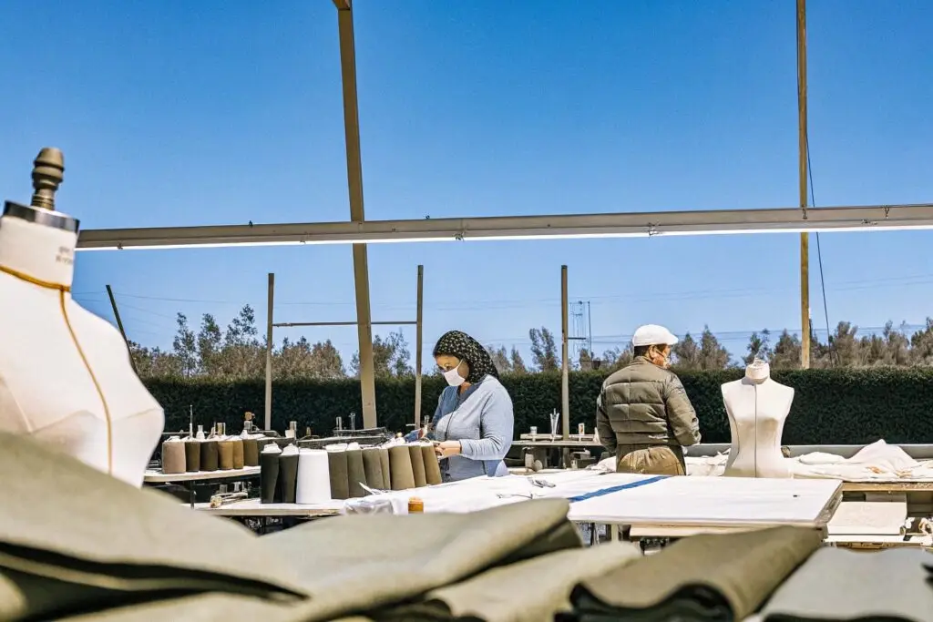 An outdoor garment production facility with workers handling fabrics and sewing near mannequins, ensuring quality craftsmanship.