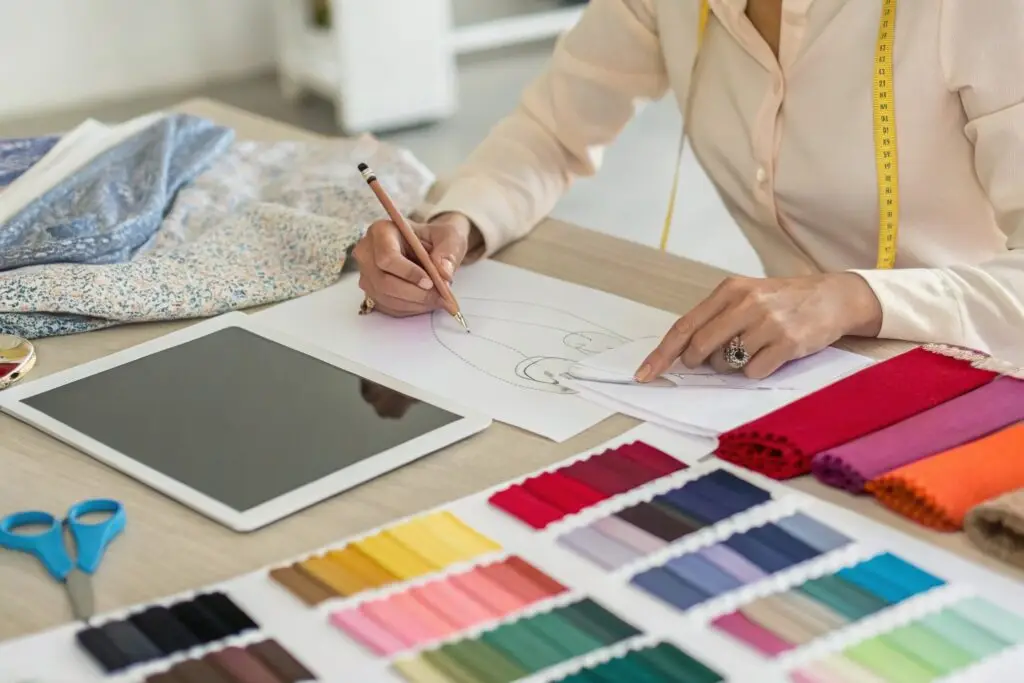 A fashion entrepreneur working at a desk, sketching designs with fabric swatches and a tablet