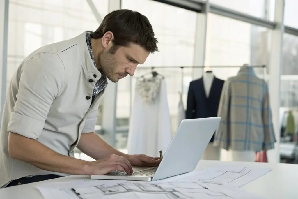 Tech pack designer working on detailed garment designs using laptop in studio
