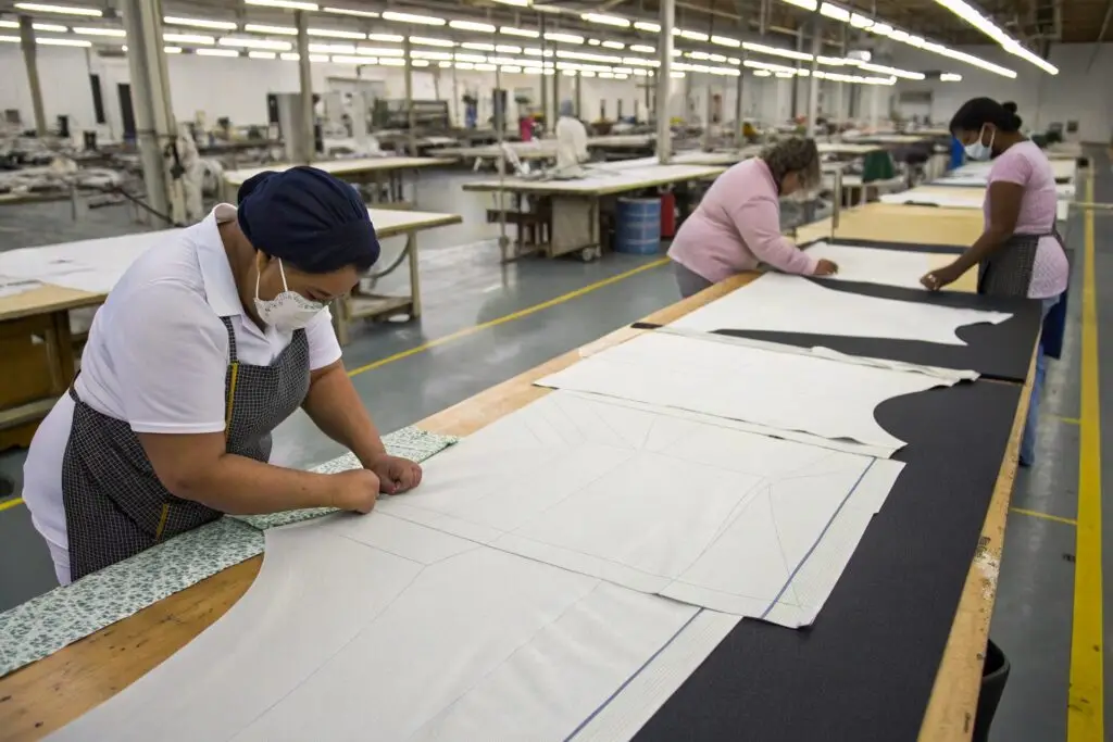 Workers at a large table in a clothing factory, arranging fabric patterns