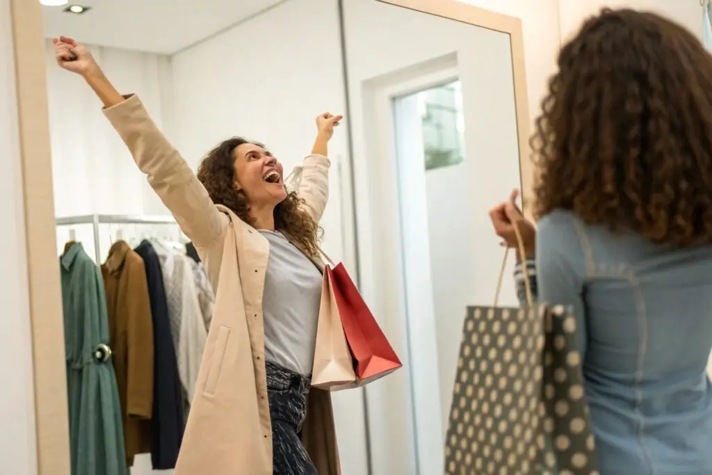 Happy woman celebrating in fitting room with shopping bags