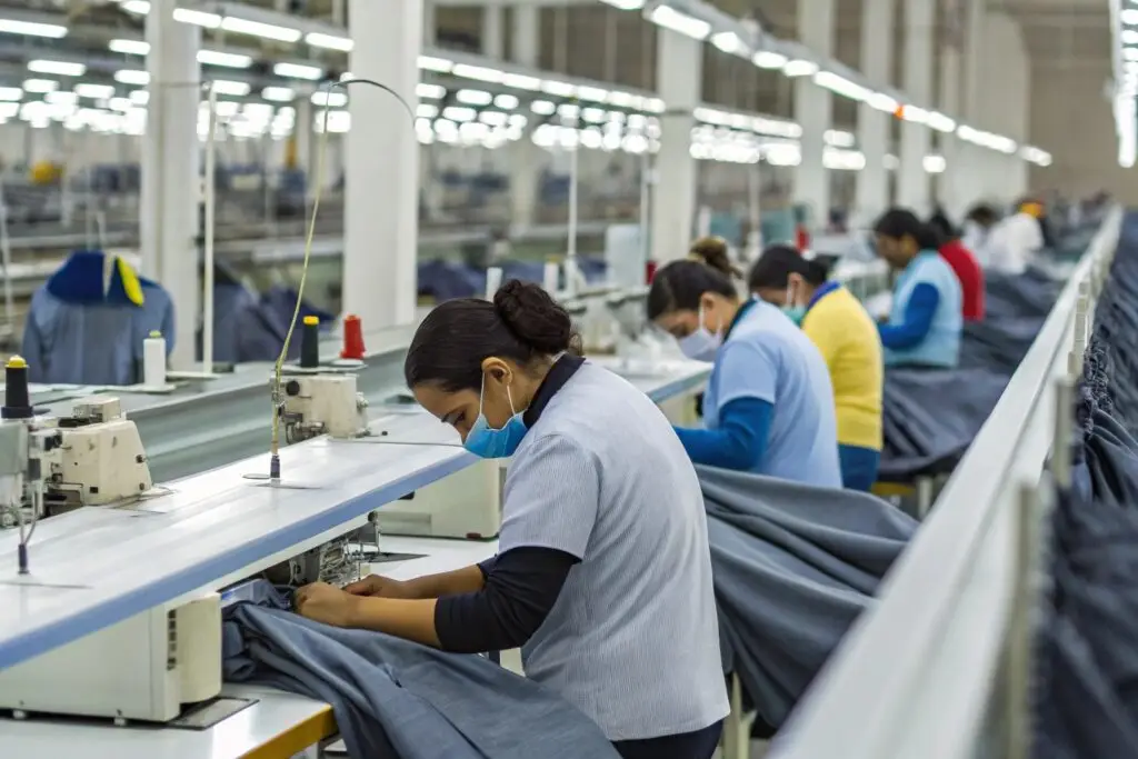 Workers in a clothing manufacturing facility sewing garments on the production line