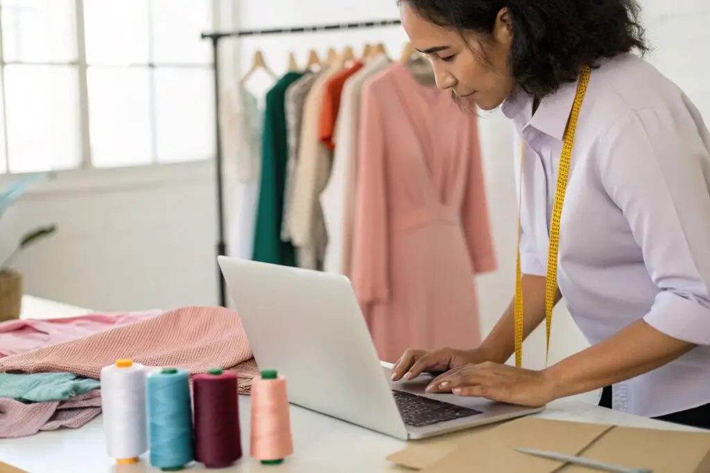 Boutique owner working on laptop with fabric samples and sewing materials