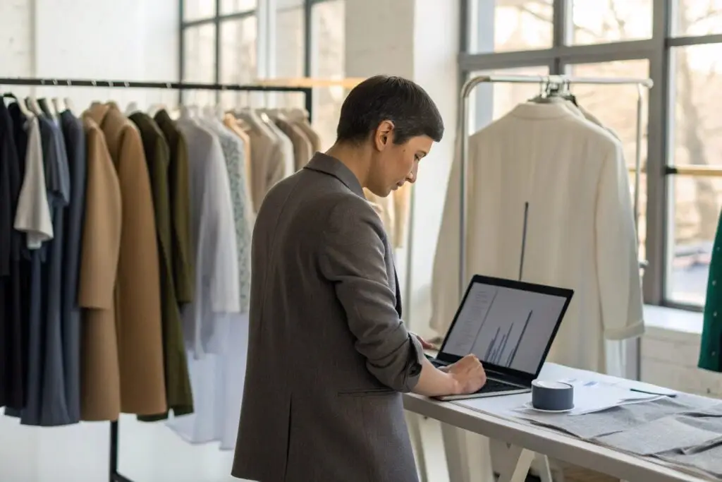 Business owner reviewing data and fashion collection on laptop in a studio
