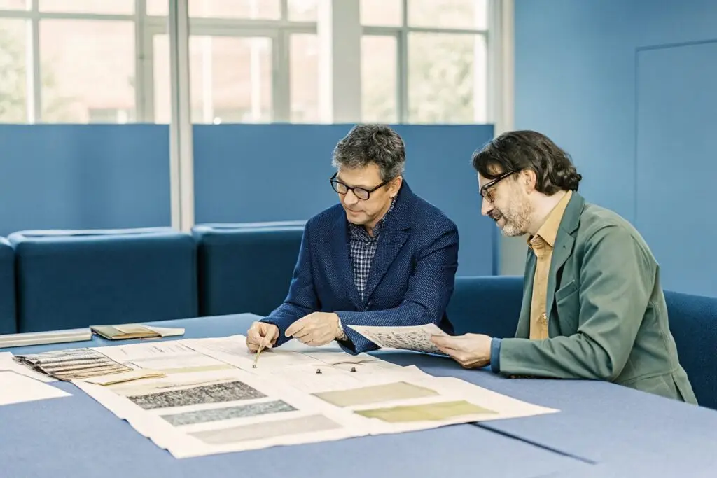 Two fashion industry professionals discussing textile patterns and production strategies.