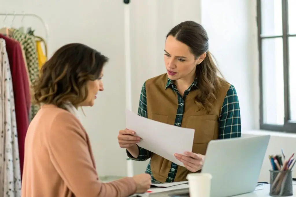 Freelance fashion designer discussing designs with a colleague in a studio