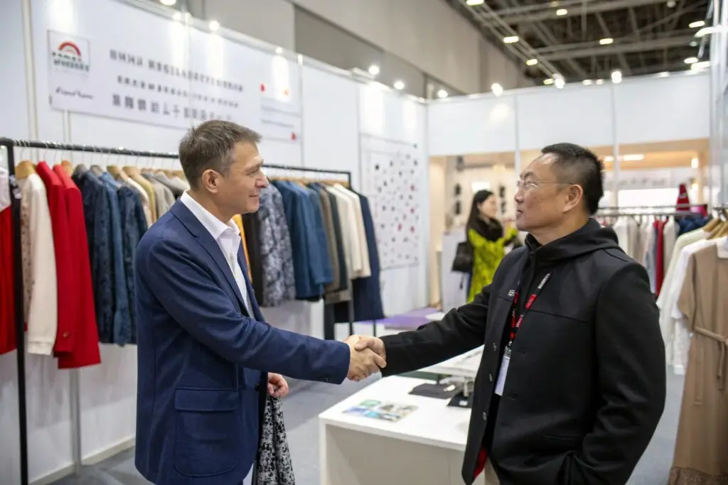 Fashion buyer and supplier shaking hands at apparel booth