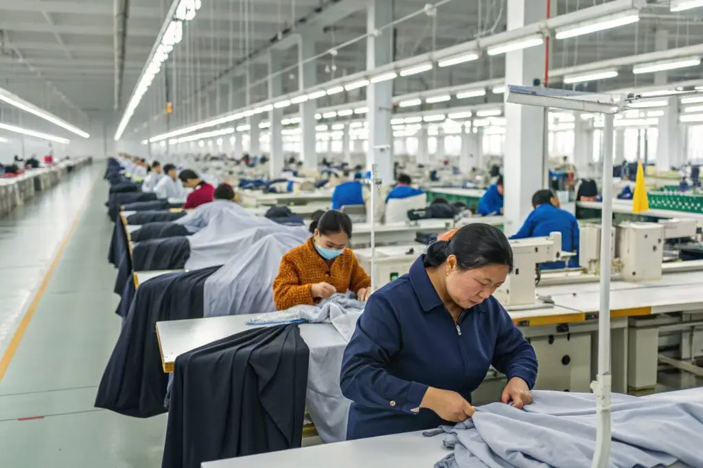 Workers in a modern Chinese clothing factory focused on sewing and fabric handling, illustrating busy production lines