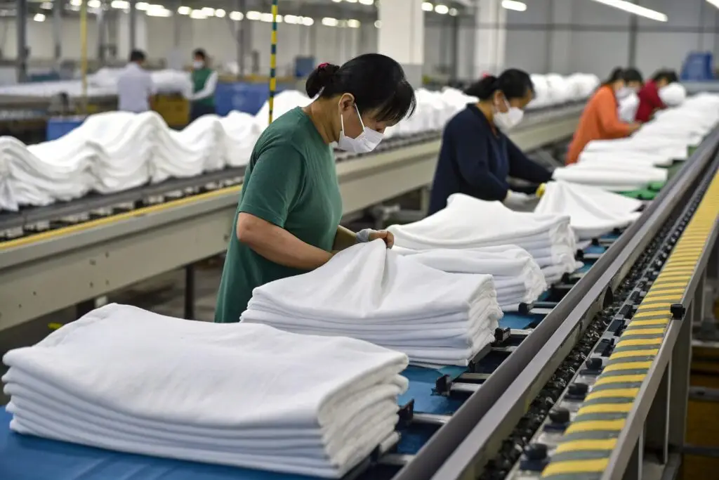Chinese garment workers folding white clothes in modern factory